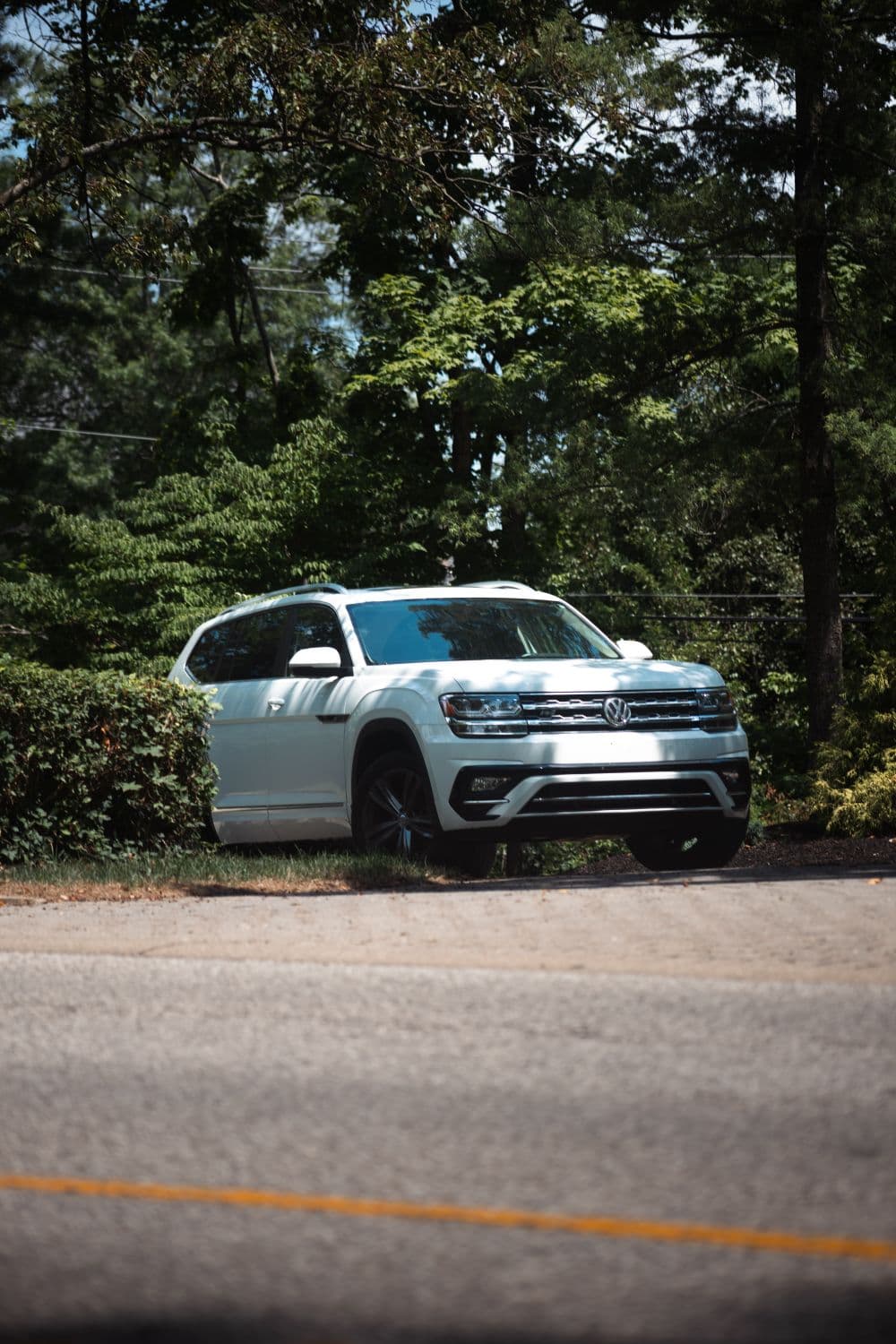 White three-row SUV parked beside a tree-lined road, similar to a Chevrolet Traverse