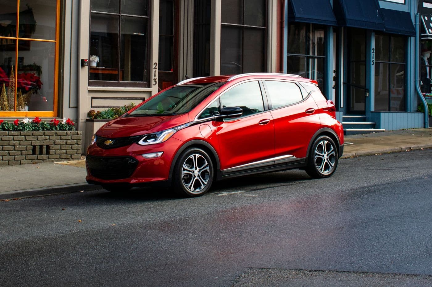 Red Chevrolet Bolt, a small Chevy hatchback, parked on a quiet street in front of shops, similar to the Chevrolet Bolt