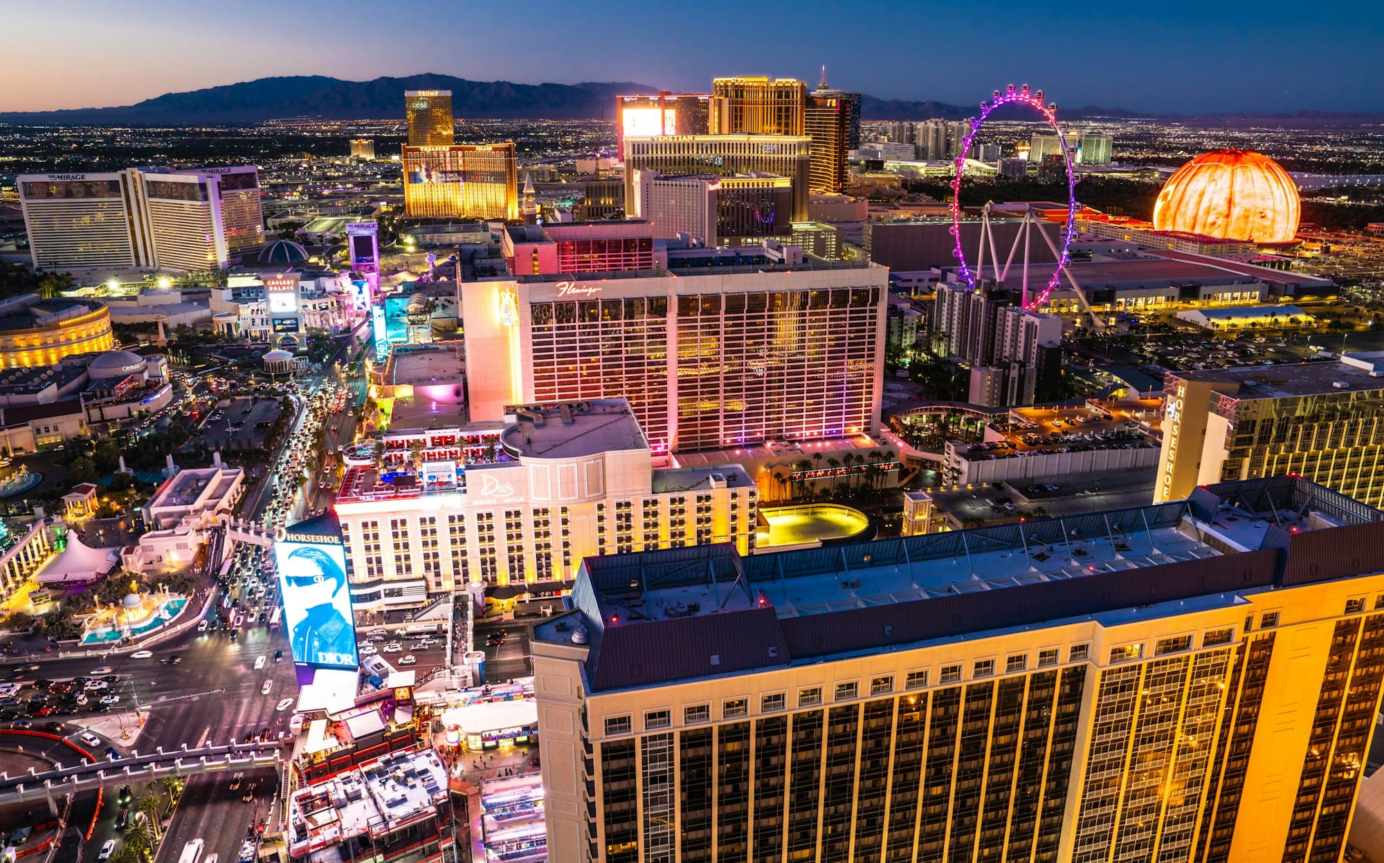 Aerial view of the Las Vegas Strip at dusk, with the hotels and the High Roller wheel lit up